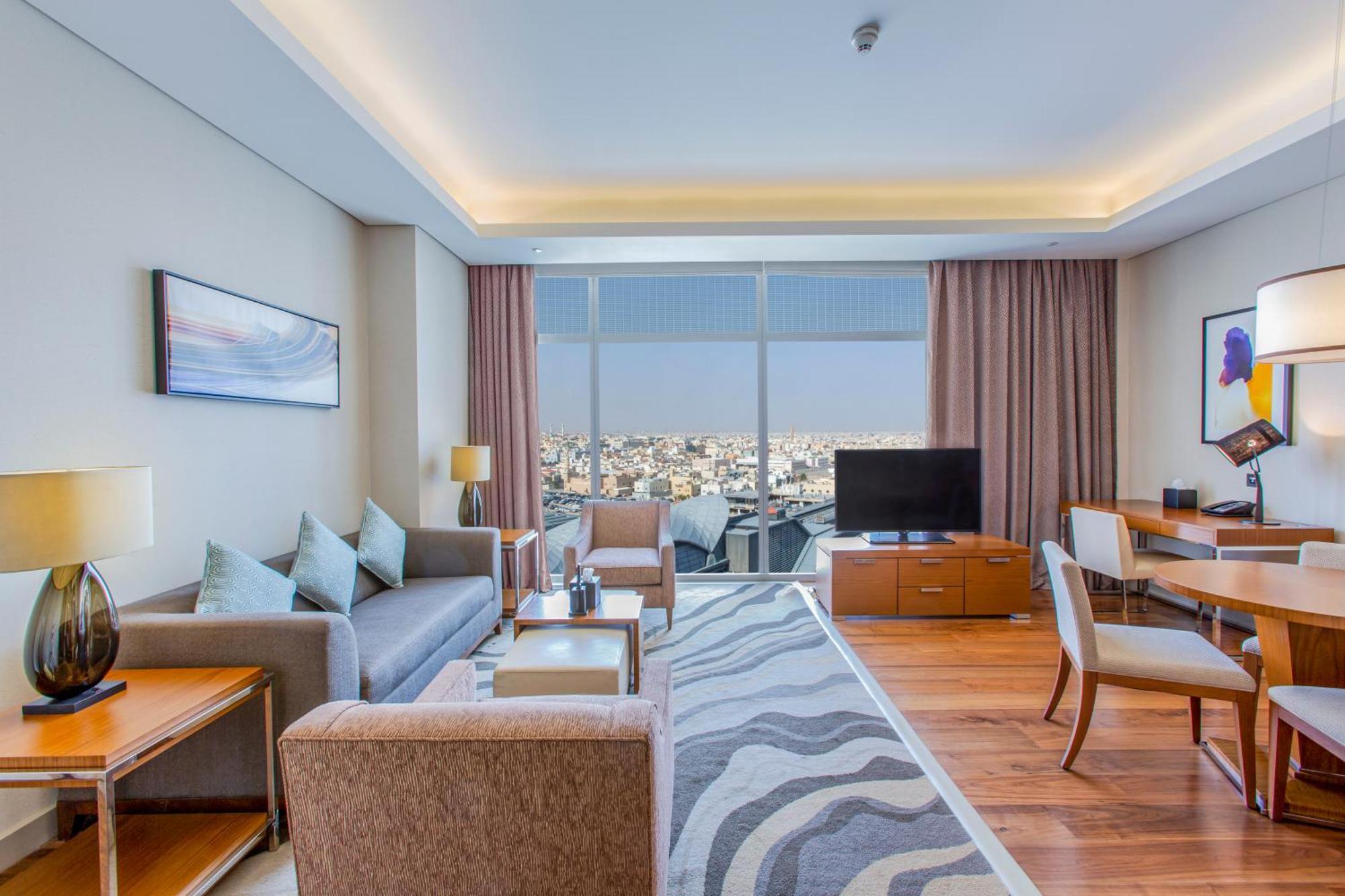 Hilton Riyadh Hotel & Residences エクステリア 写真 The photo shows a modern hotel room or suite. The space features a stylish living area with a sofa and armchairs arranged around a coffee table. There are lamps providing ambient lighting, and a large window offers a view of the cityscape outside. A 