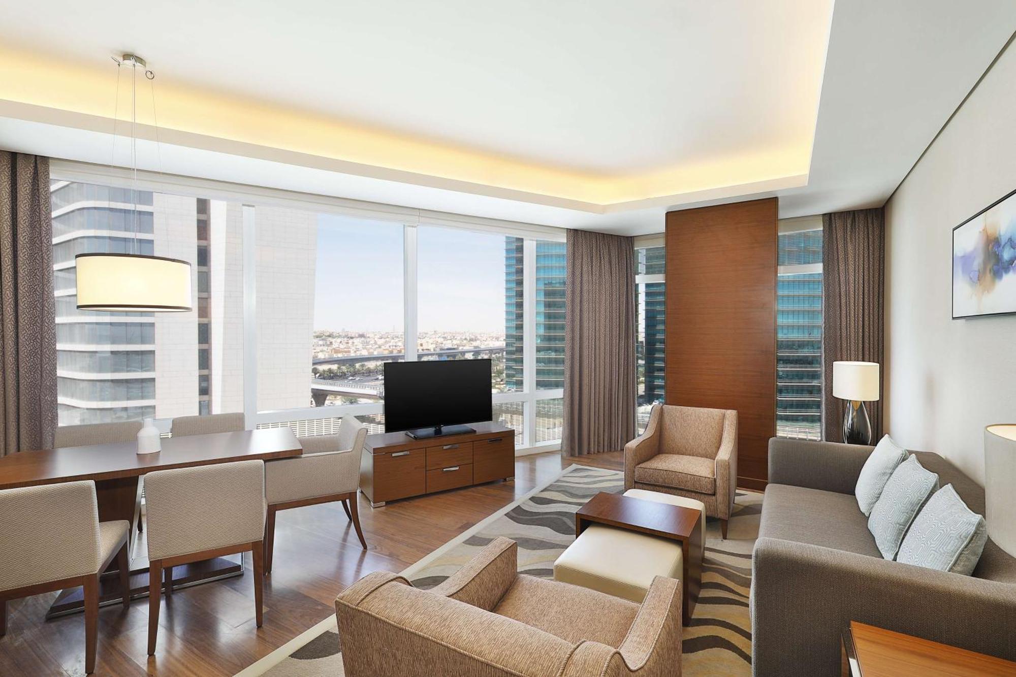 Hilton Riyadh Hotel & Residences エクステリア 写真 The image shows a modern, stylish living area in an apartment or hotel suite. It features large windows that provide a view of the cityscape, allowing natural light to flood the space. The furnishings include a comfortable sofa, armchairs, and a coff