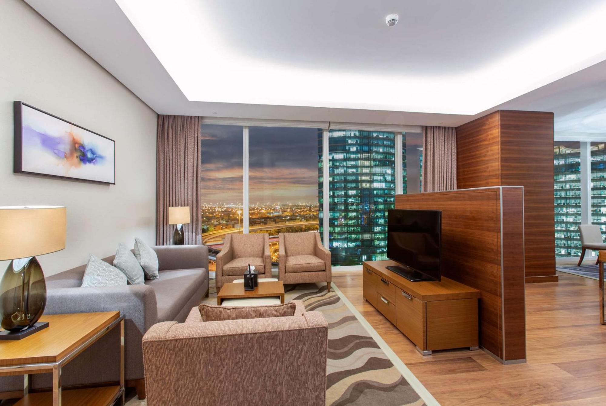 Hilton Riyadh Hotel & Residences エクステリア 写真 The photo shows a modern living room in a stylish apartment. The space features a comfortable seating arrangement with a light gray sofa and two brown armchairs, complemented by a wooden coffee table. There is a large flat-screen TV mounted on a wood