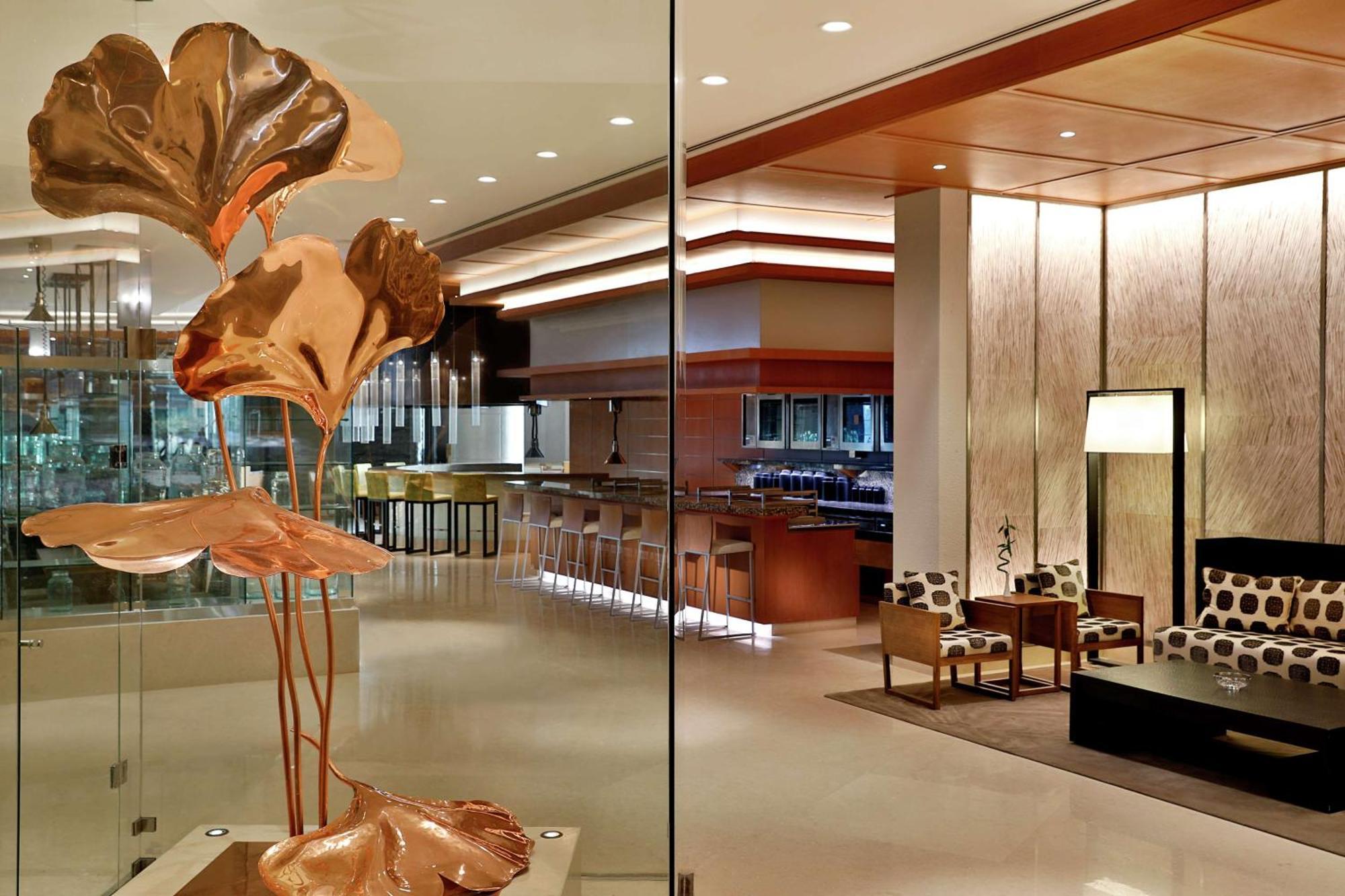 Hilton Riyadh Hotel & Residences エクステリア 写真 The photo depicts a modern and stylish interior space, likely a hotel lobby or upscale lounge. In the foreground, there is an artistic sculpture of copper-colored leaves or flowers, adding an elegant touch. The background features a well-lit bar area