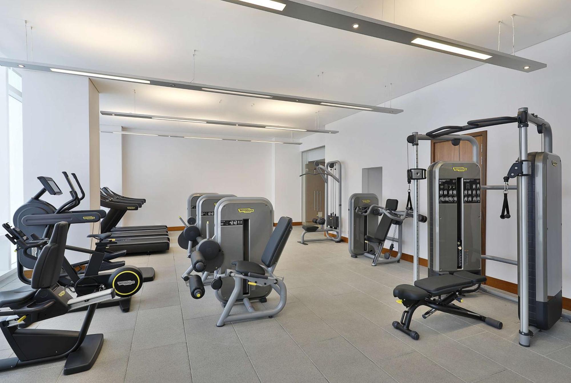 Hilton Riyadh Hotel & Residences エクステリア 写真 The photo shows a modern gym or fitness center with various exercise equipment. On the left, there are several treadmills, while the center features a range of weight machines. There is a multi-station gym equipment, and a bench press is also visible